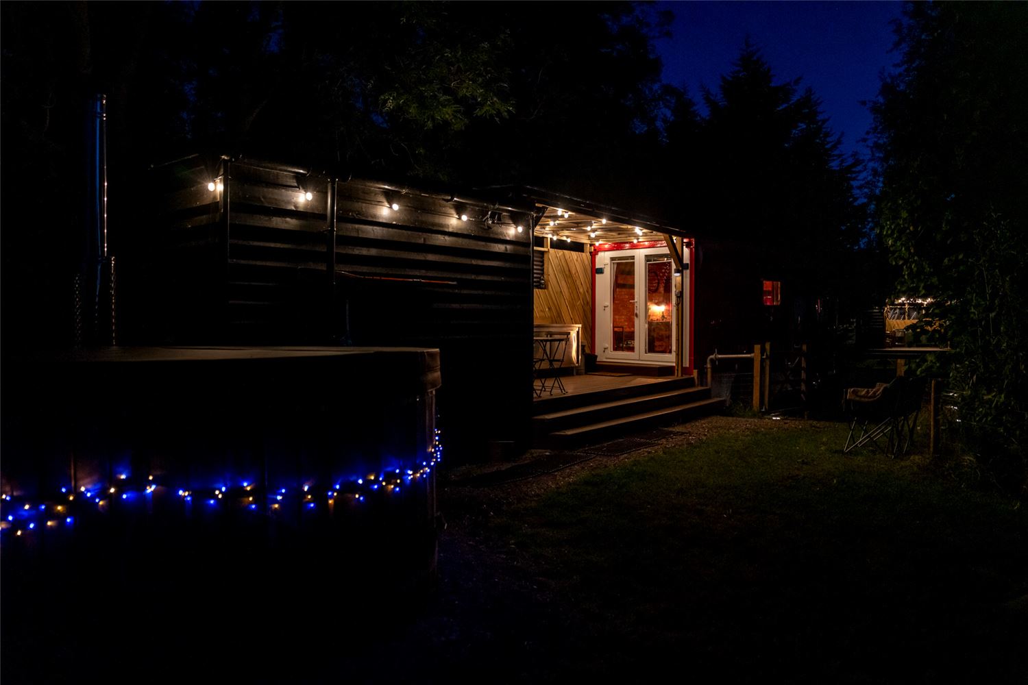 Three girls laughing in a wood fired hot tub surrounded by trees.
