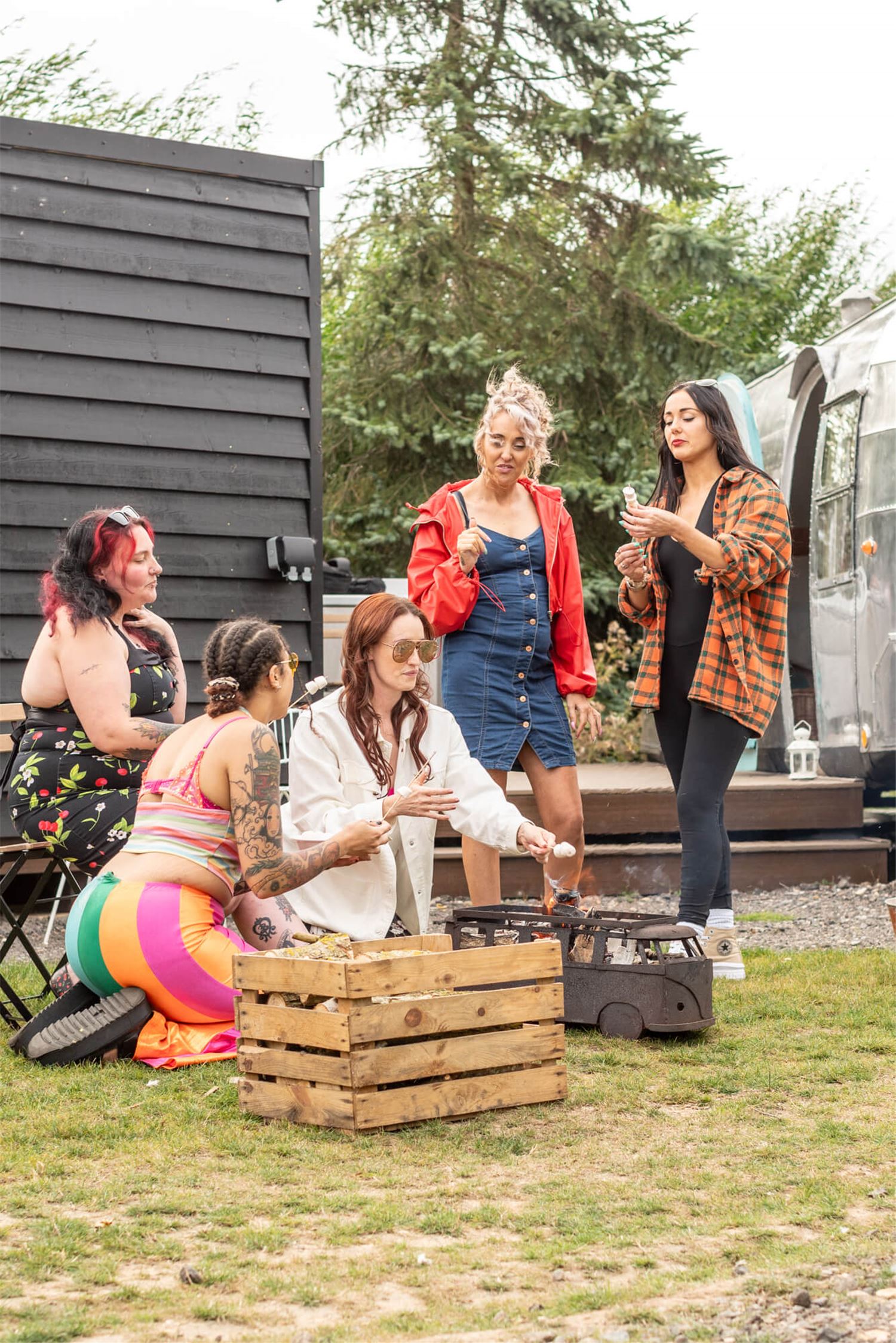 Guests  in front of an Airstream, toasting marshmallows over a VW camper shaped fire pit.