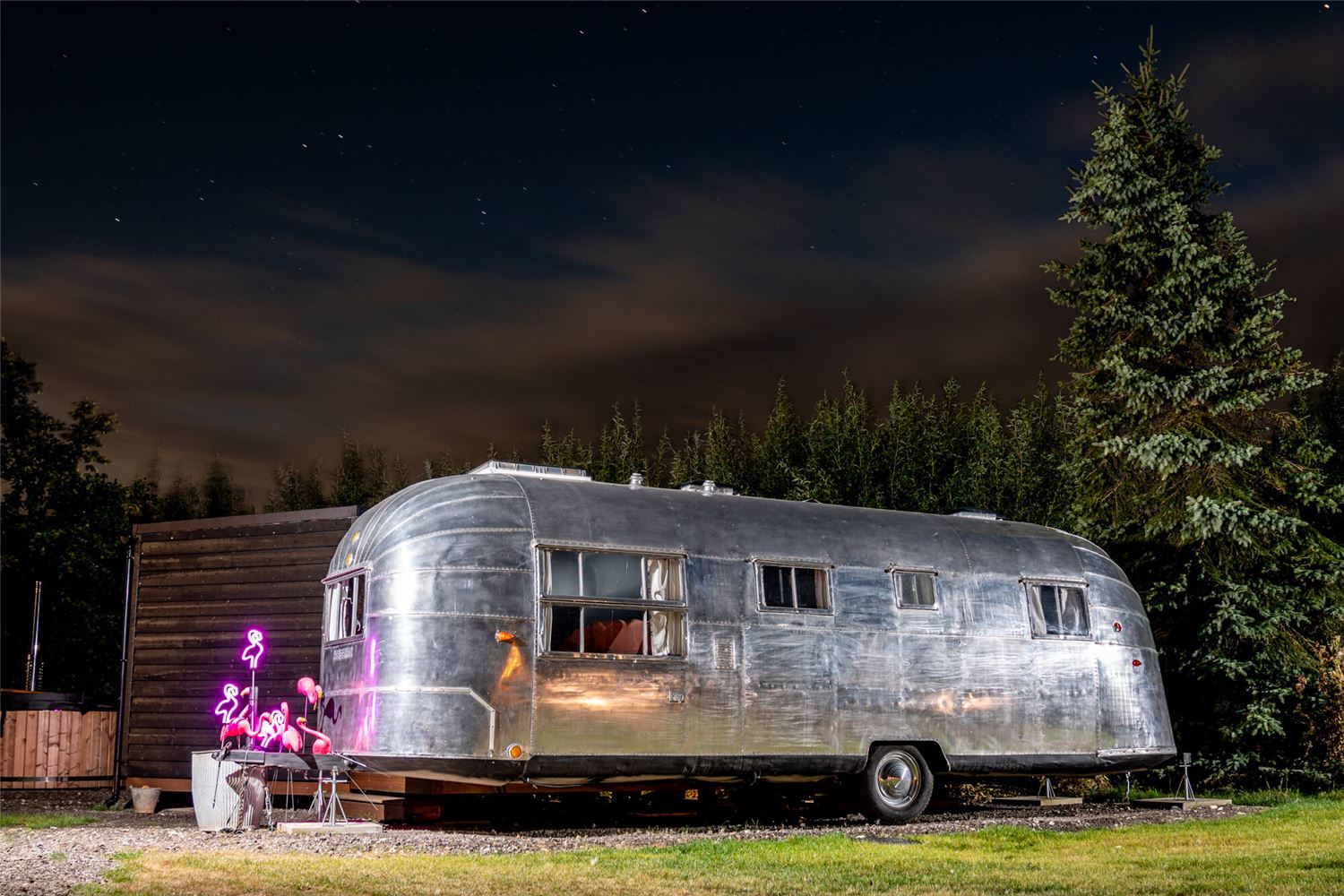 Peggy Sue, a silver Airstream shown at night with neon pink flamingo lights.