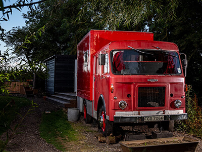 Dennis, a red fire engine shown at night surrounded by trees.