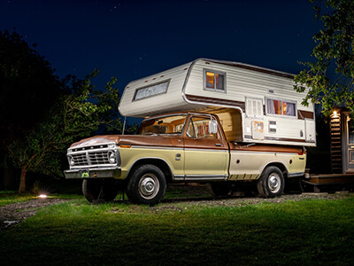 Willy, a yellow and brown truck with a camper shell attached, at night.